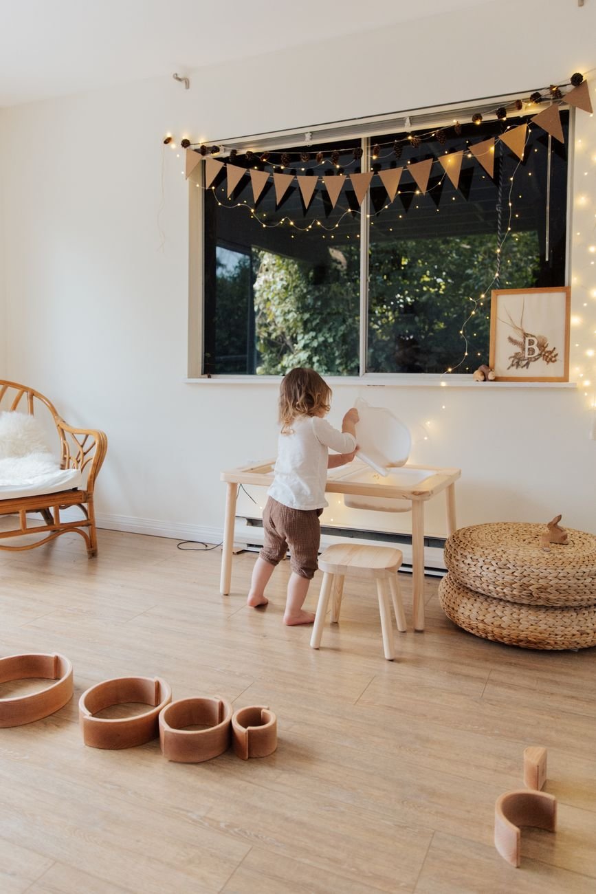 A child playing in a cozy, decorated indoor playroom with wooden toys and warm lighting.