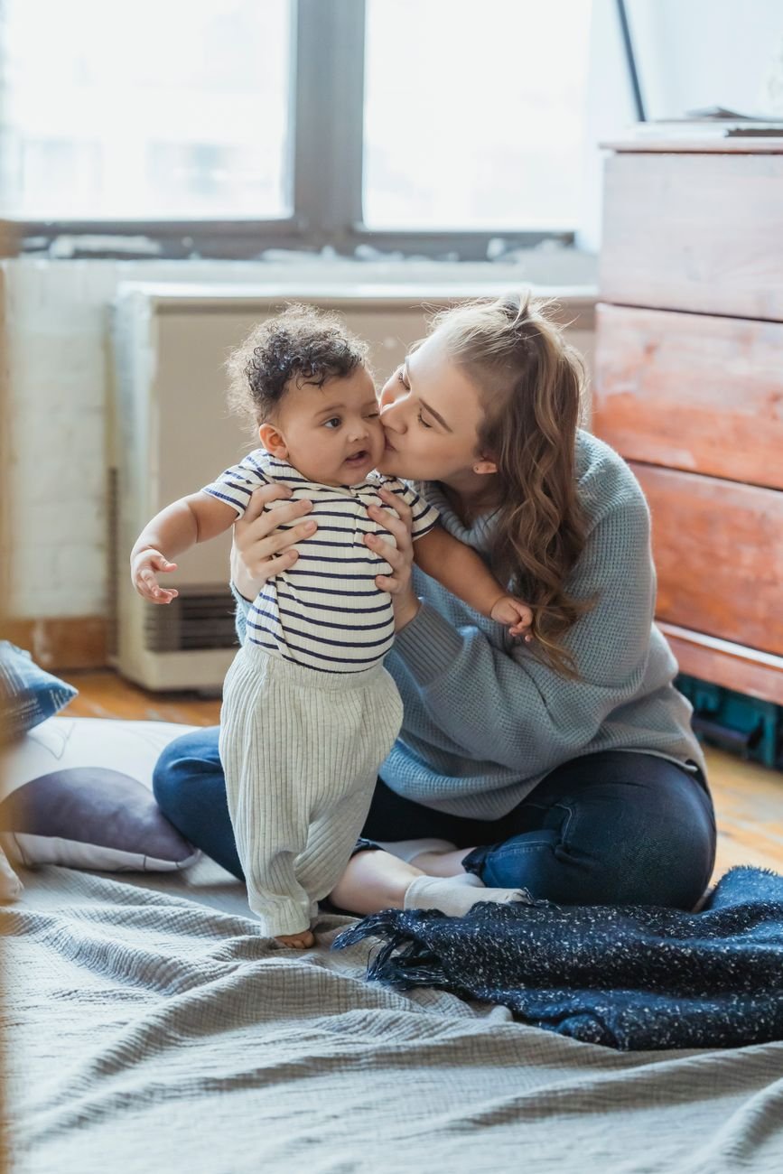A warm, caring mother holding and kissing a young child at home, capturing a gentle and nurturing moment.